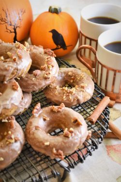 several vegan pumpkin pecan donuts with maple cinnamon glaze on cooling rack with coffee, cinnamon sticks and pumpkins