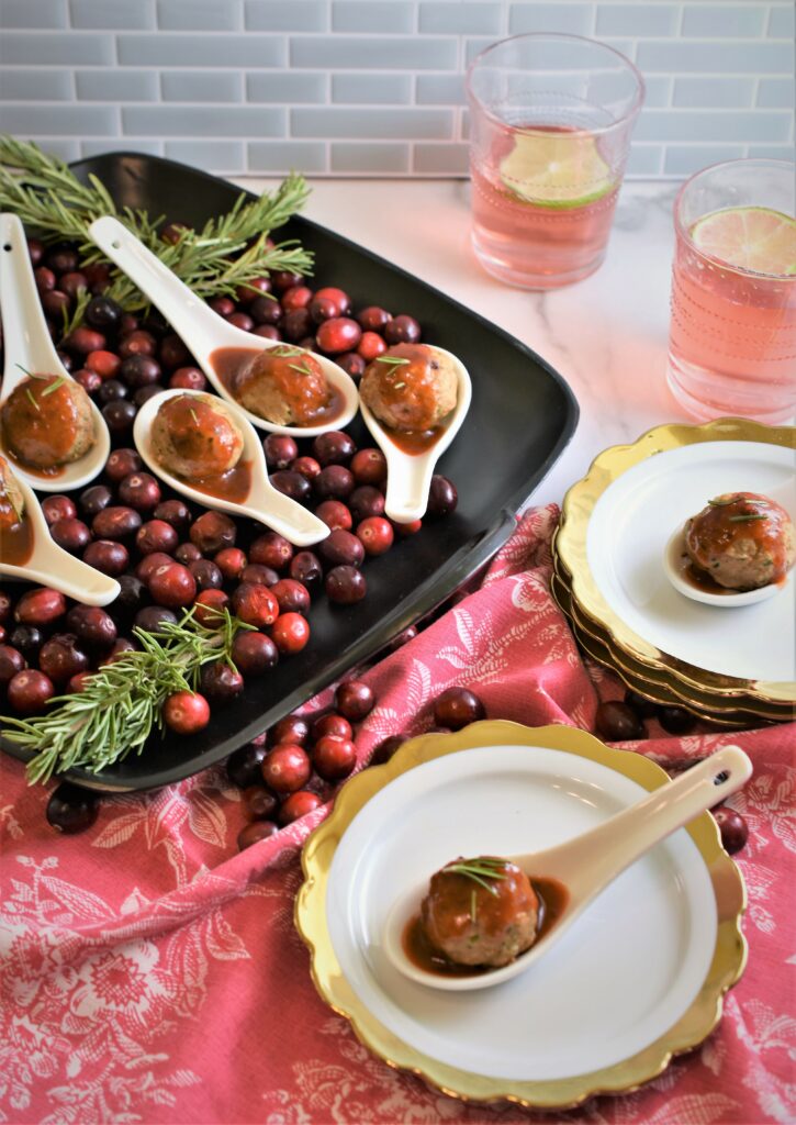 cocktail turkey meatballs in spoons on a bed of fresh cranberries in black ceramic platter
