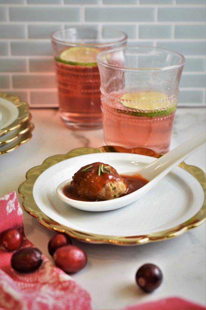 white and gold appetizer plate with cranberry turkey meatball on white marble countertop with cocktails in the background