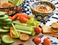 chipotle almond dip in black and white dip bowl with veggies and crackers in black wire basket and on cutting board