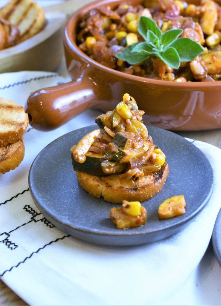 zucchini corn relish on toast in small black plate with bowl garnished with fresh oregano 