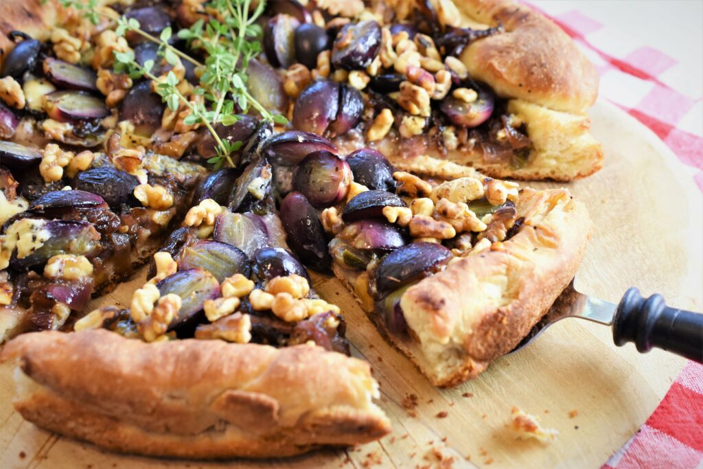 skillet black grape pizza with gorgonzola and walnuts with fresh thyme on wood cutting board red and white checkered napkin with a black marbled handled pie server