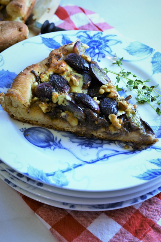 a serving of one slice of black grape pizza on a stack of blue and white floral plates 