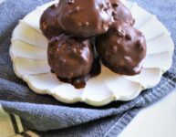 half a dozen peanut butter s'more bombs on a scalloped cream colored ceramic dessert plate on a denim and white striped towel on marble counter top