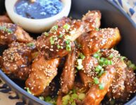 up close image of black serving casserole of chicken wings with sesame apricot sauce in dip bowl