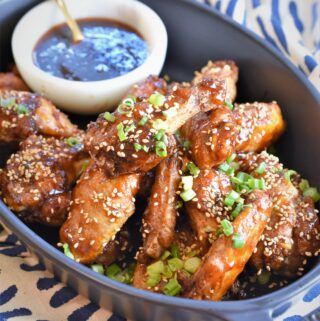 up close image of black serving casserole of chicken wings with sesame apricot sauce in dip bowl