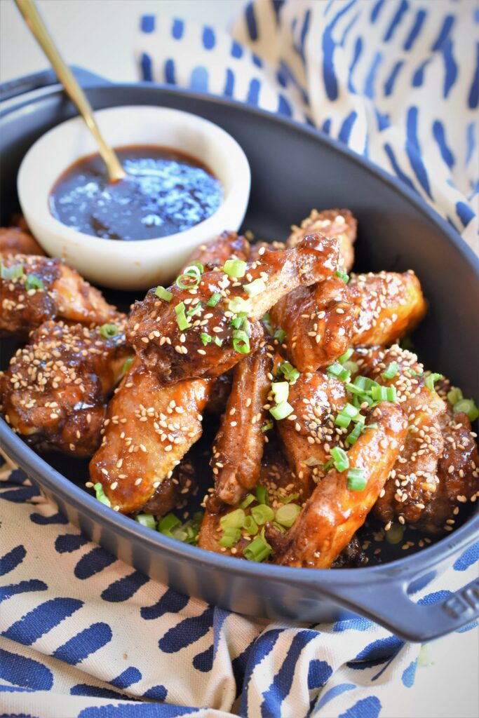 up close black casserole filled with chicken drumettes along with dip sauce in a small bowl on blue and white contemporary patterned cloth napkin