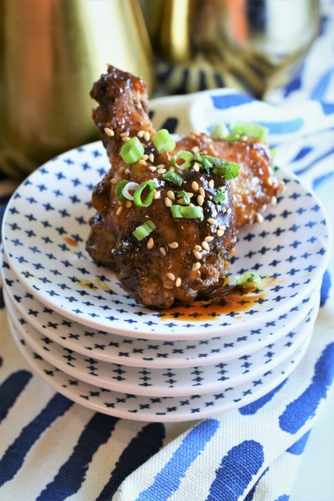 green onions and sesame garnished chicken on a stack of appetizer plates 