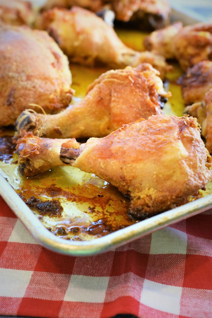 sheet pan right out of the oven with oven fried chicken on it placed on a red and white checkerboard tablecloth