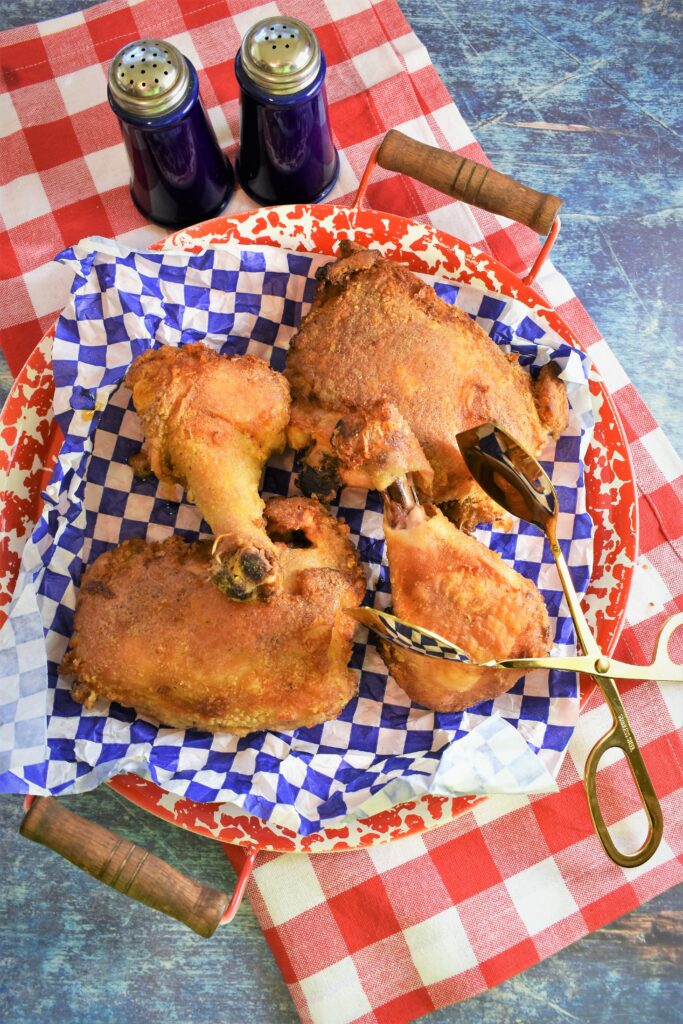 view from above with red and white platter with blue and white checked paper with crispy oven baked legs and thighs on it with large gold serving tongs