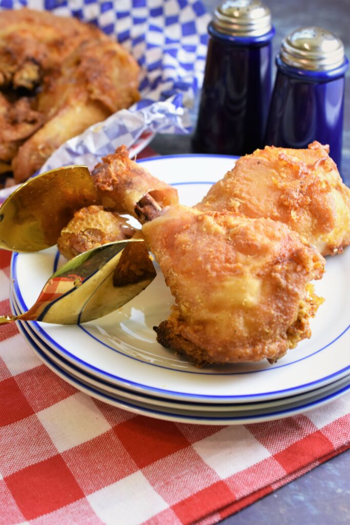 two chicken legs on a stack of white and blue plates on a red and white checked napkin with cobalt blue ceramic salt and pepper shakers in the background