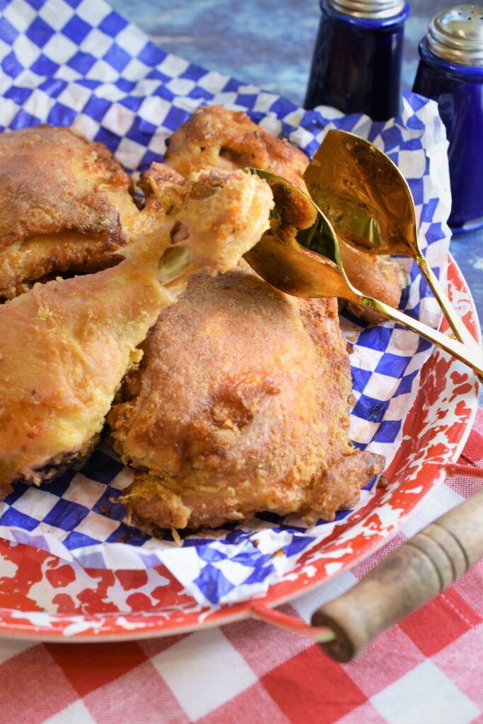 up close red and white speckled metal platter with several pieces of oven fried chicken with gold serving tongs