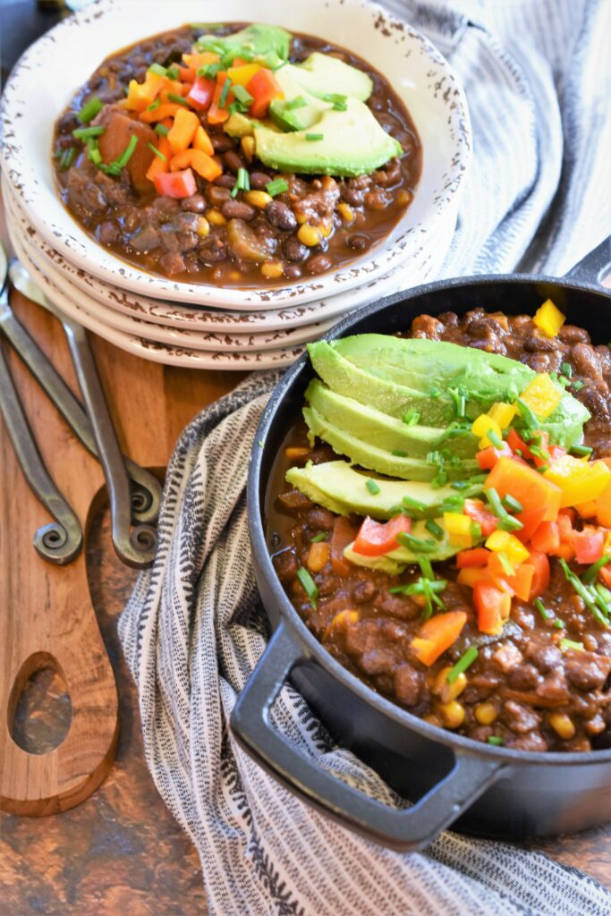 cutting board with black and white country towels with stacked chili bowls and a large iron pot

