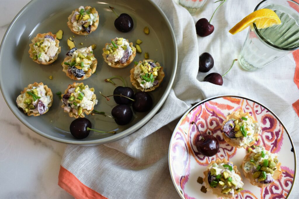 overhead shot of fresh cherries with salmon colored trimmed gray linen napkin, gray serving platter along with appetizer plates with small bites 