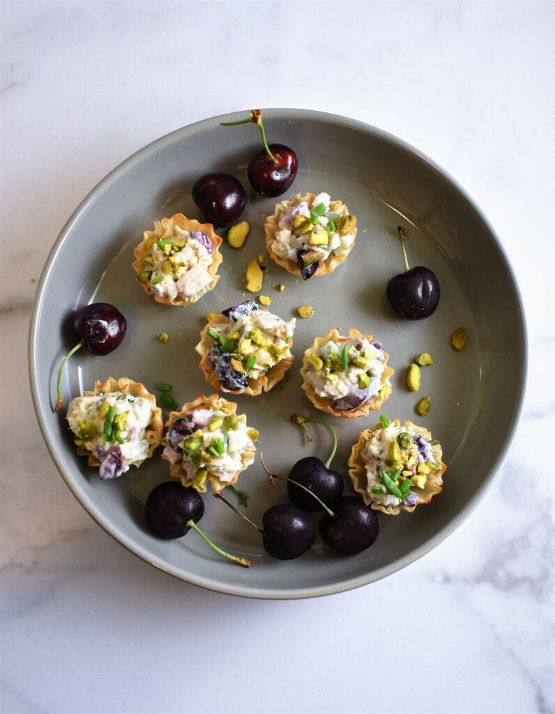 overhead view of gray round ceramic platter with chicken salad tarts with Gorgonzola, pistachios & cherries