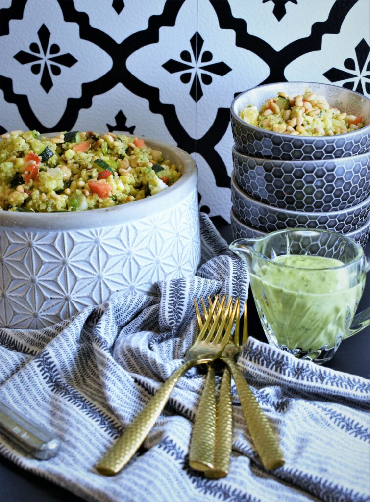 garden fresh zucchini quinoa salad with corn & sun-dried tomatoes in large concrete bowl with gold forks off to the side with a small pitcher of basil vinaigrette 