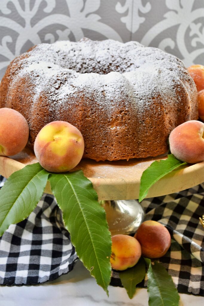 bundt cake sprinkled with powdered sugar on a cake stand garnished with fresh peaches
