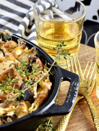 up close photo of two glasses of chardonnay next to dinner in baking dish with two gold forks on wood rustic board