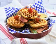 Jalapeno Cheddar Cornbread BLT Waffles in round red quiche dish on blue and white checkered paper with little white scalloped dish with Dijon honey mustard mayo spread