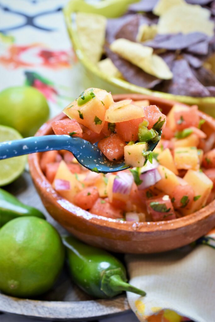 up close image of a light blue and white speckle ware spoon of dip from a bowl of salsa below