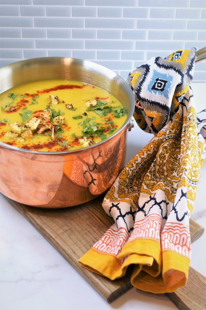 copper pot of soup with cloth napkin wrapped around handle