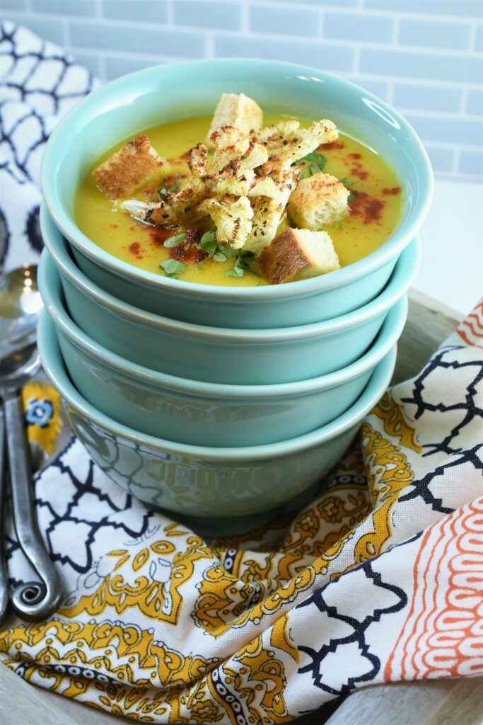 stack of 4 sea green bowls with curried cauliflower & apple soup in the top one