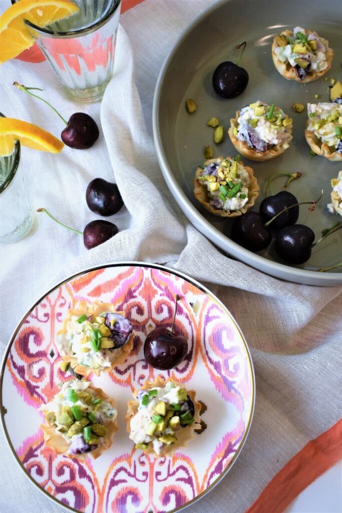 chicken salad phyllo cups in round gray dish next to small appetizer plate