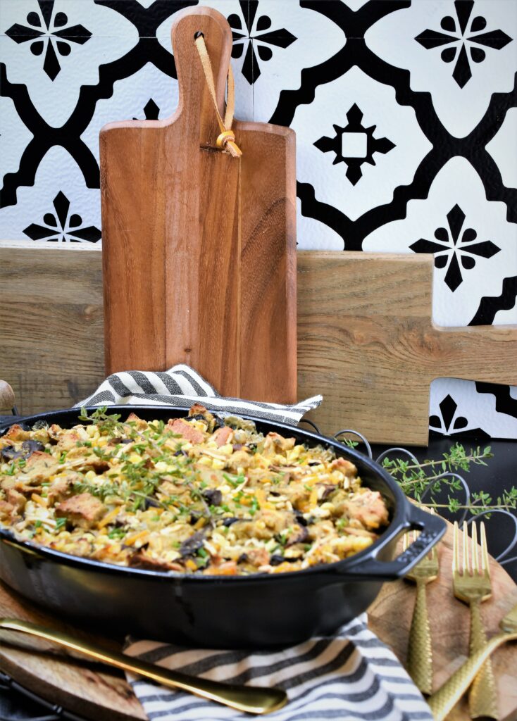 vegan bread pudding with mushrooms and corn on an oval wire edged wood tray on black counter top with two cutting boards leaning against a black and white patterned back splash