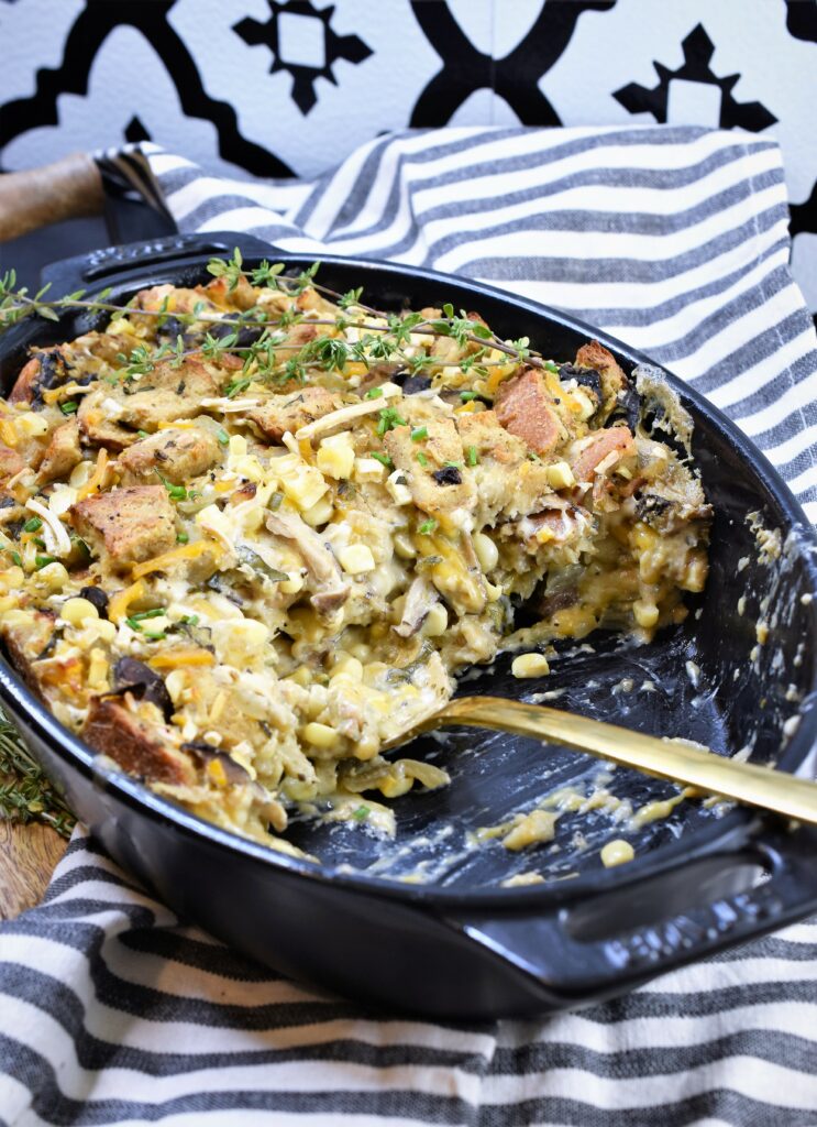 vegan bread pudding with mushrooms and corn in an oval black casserole half gone on grey and white striped kitchen towel