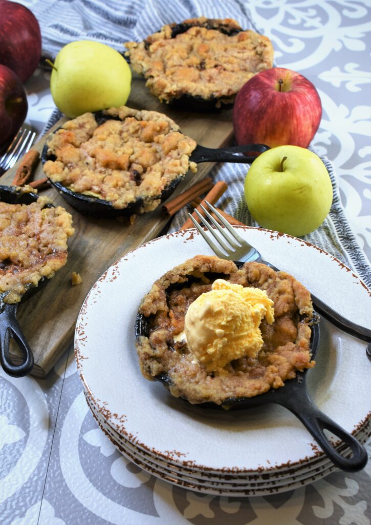 set of 3 skillet desserts on wood cutting board with one on stack of plates next to it