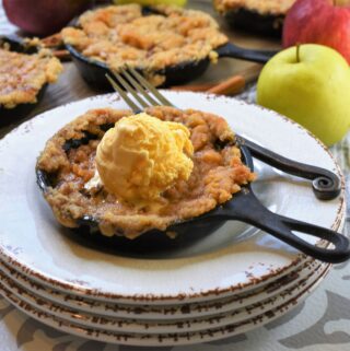 up close image of skillet snickerdoodle apple crisp on a stack of four white rustic plates with iron handled fork