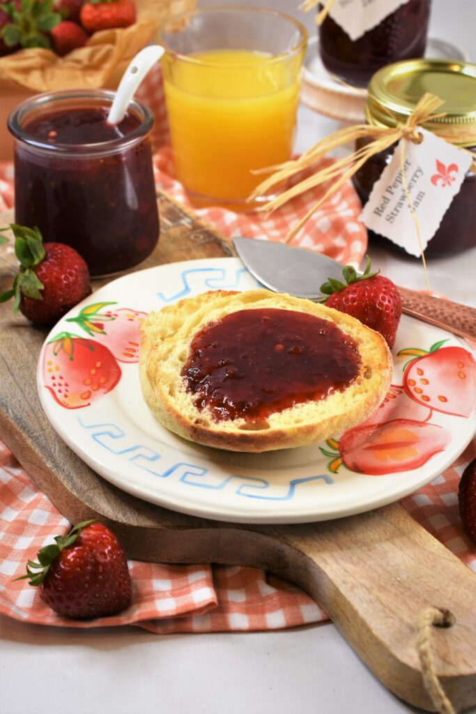 English muffins spread with jam on plate displayed on cutting board with copper knife on the side