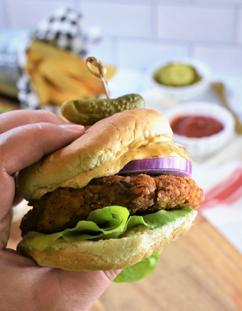 up close hand holding one Chipotle Butternut Squash Burger with Hatch Chile Aioli