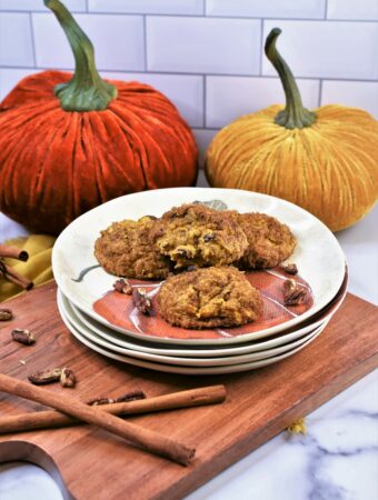 pumpkin pecan cookies on a stack of autumn inspired plates on cutting board with velvet pumpkins in the background