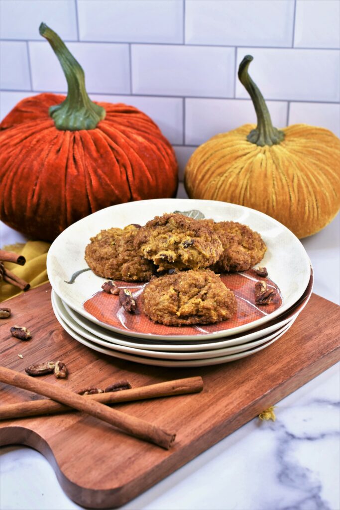 pumpkin pecan cookies on a stack of autumn inspired plates on cutting board with velvet pumpkins in the background