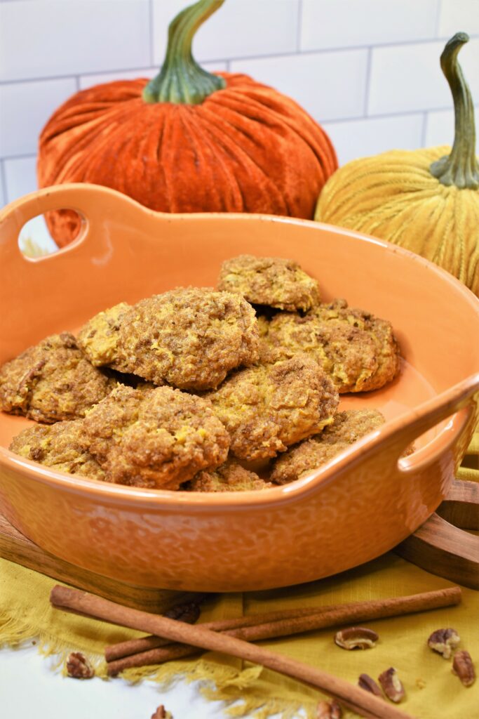 quick vegan pumpkin cookies with pecans and cinnamon in orange ceramic dish with velvet pumpkins in the background