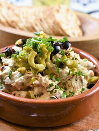 olive sun-dried tomato cream cheese dip in terracotta dish on wood board