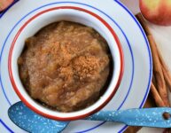 brown sugar spiced applesauce in white and red enameled bowl on blue and white sauce with apples in the background