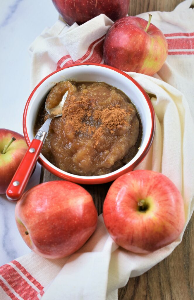 brown sugar spiced apple sauce focused from above in white and red bowl with red handled spoon and many fresh McIntosh apples