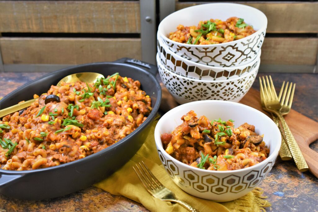vegan chorizo Mexican goulash in black casserole staub dish with gold and white bowls off to the side with gold forks