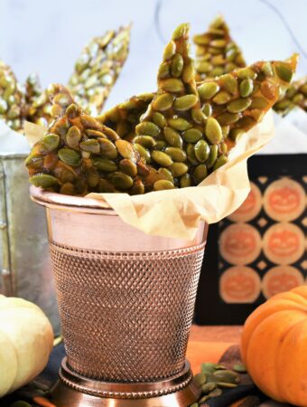 vegan pumpkin seed brittle in mini metal Halloween treat containers with mini pumpkins surrounding