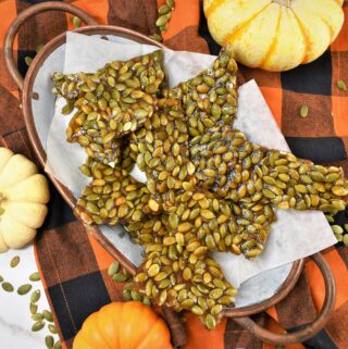 pumpkin seed brittle on oval rustic copper tray on black and orange buffalo plaid napkin with mini pumpkins surrounding