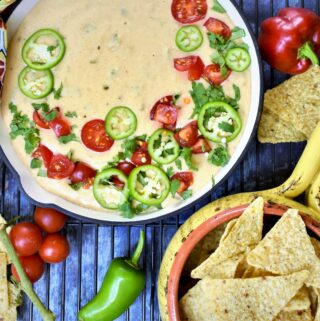 Hatch Chile Queso Blanco served in a red cast iron skillet with colorful napkin tied around handle with fresh cherry tomatoes and sliced jalopenos with tortilla chips