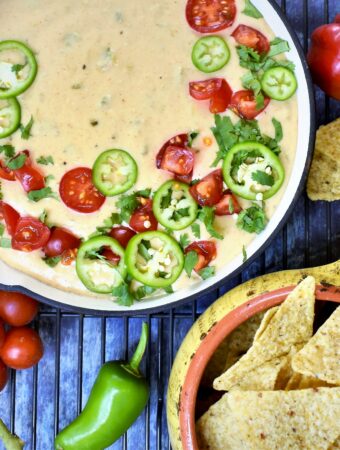 Hatch Chile Queso Blanco served in a red cast iron skillet with colorful napkin tied around handle with fresh cherry tomatoes and sliced jalopenos with tortilla chips