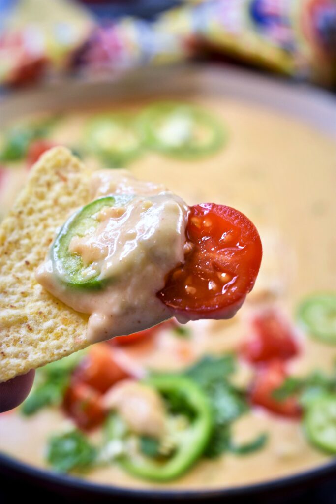 Hatch chile queso blanco scooped onto tortilla chip with jalapeno slice and cherry tomato slice