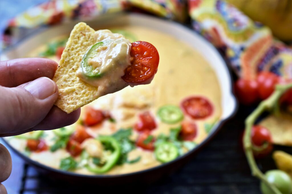 Hatch chile queso blanco scooped onto tortilla chip with jalapeno slice and cherry tomato slice