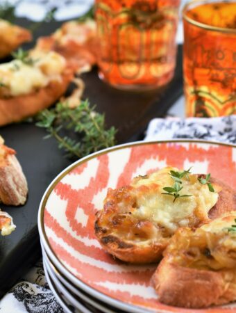 broiled cheese bruschetta on a stack of colorful appetizer plates