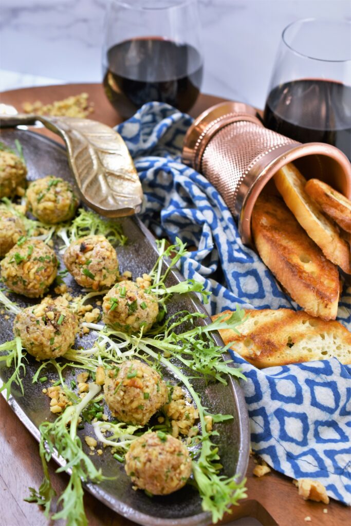 fig blue walnut truffles in dark metal dish with brass leaf with red wine in the background