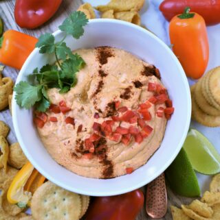 chili pepper cheese dip in white bowl with chips, crackers and veggies for dipping