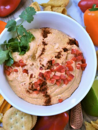 chili pepper cheese dip in white bowl with chips, crackers and veggies for dipping